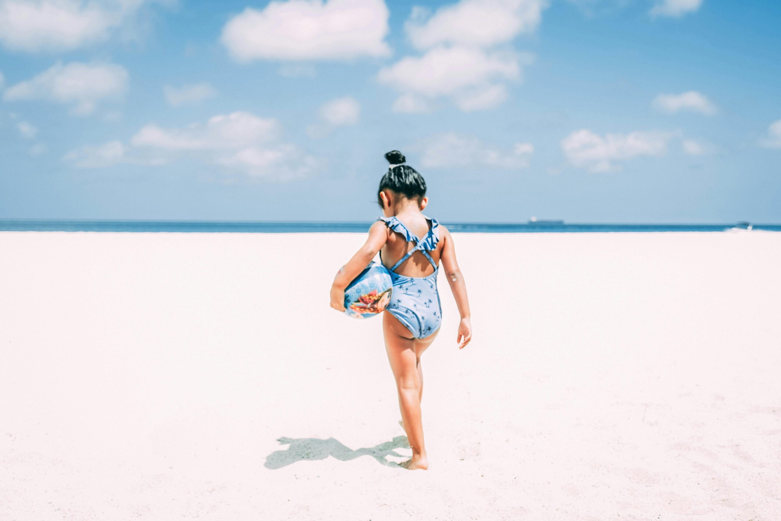 A little girl in a swimsuit enjoys a sunny day on a bright sandy beach in Aruba.