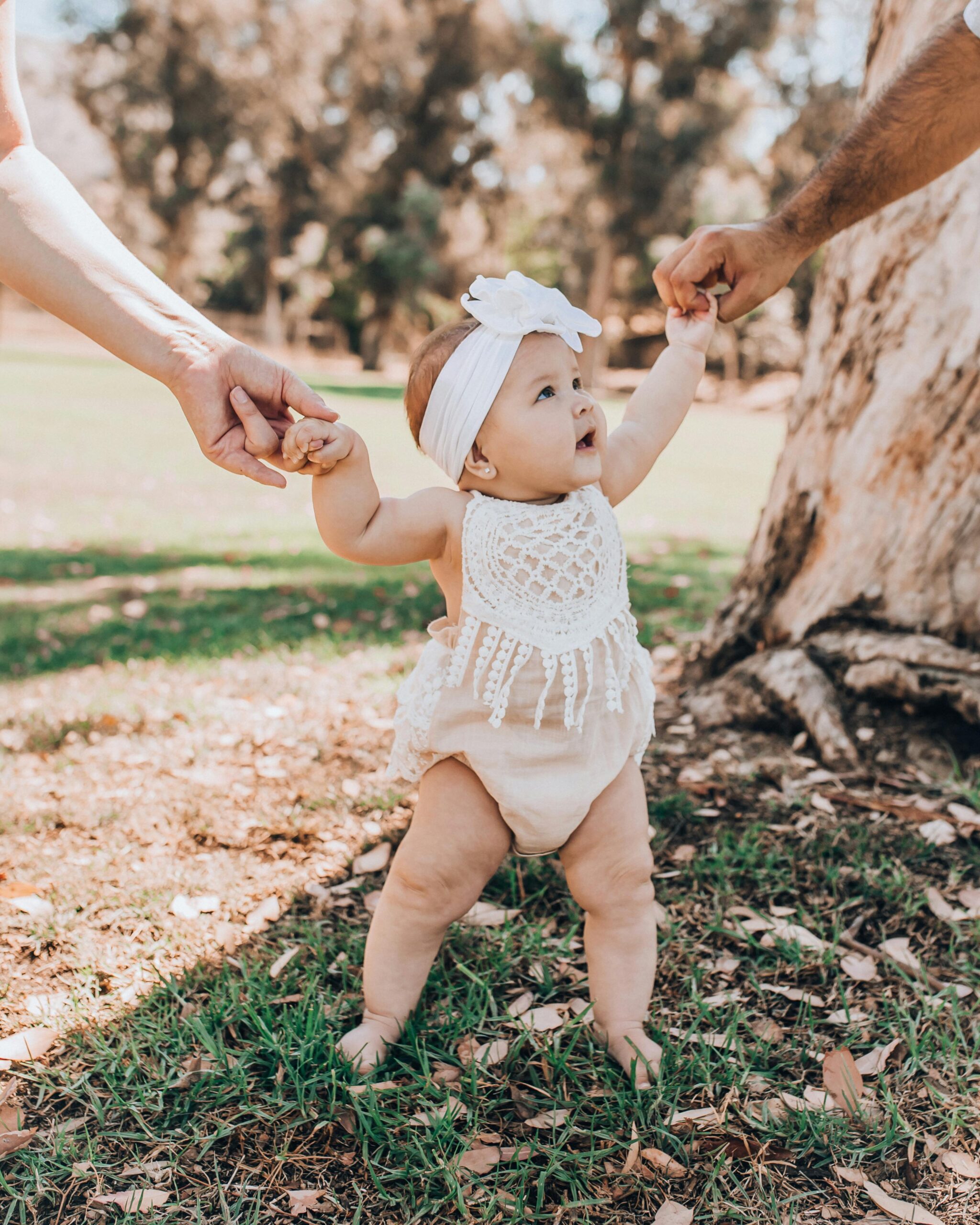 Cute baby girl learning to walk with support in a sunny Los Angeles park.