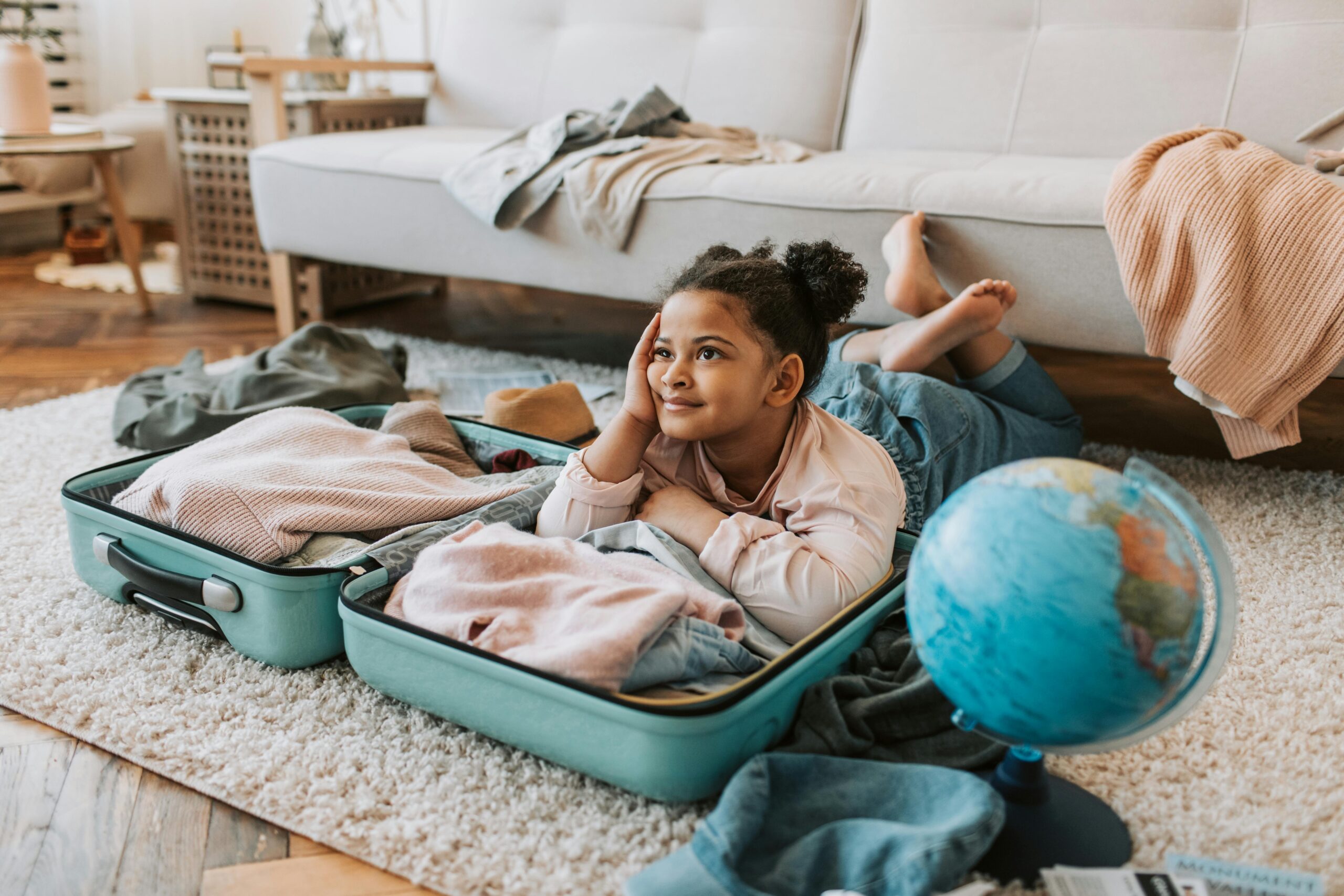 Young girl daydreams about travel, lying inside an open suitcase with clothes.